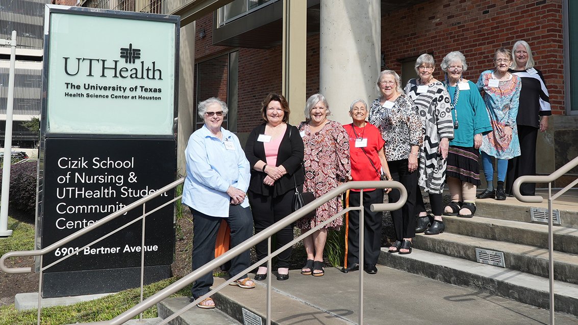 Group of women posing on the front steps beside a UTHealth Houston Cizik School of Nursing and Student Community Center sign.