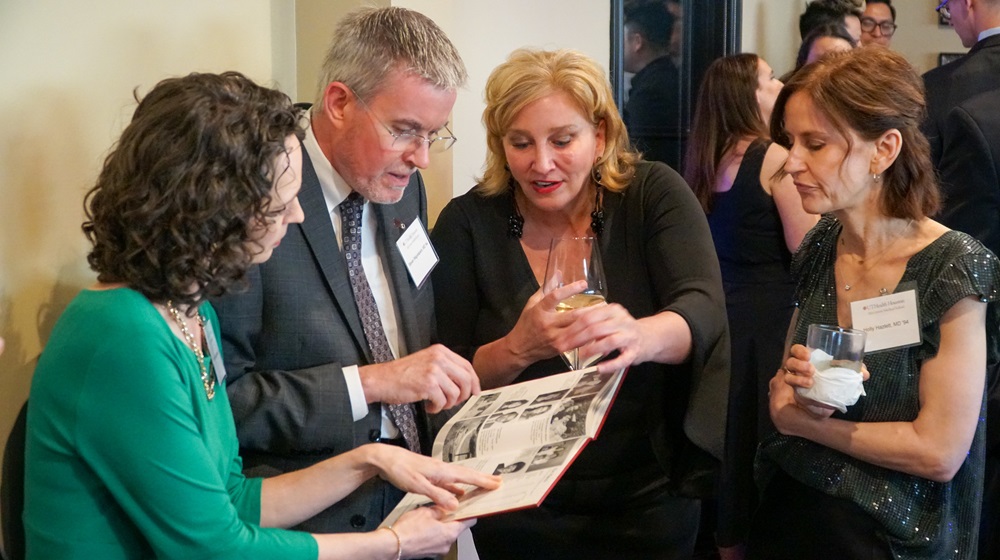 Four McGovern Medical School alumni looking at a photo album at Alumni Weekend event.