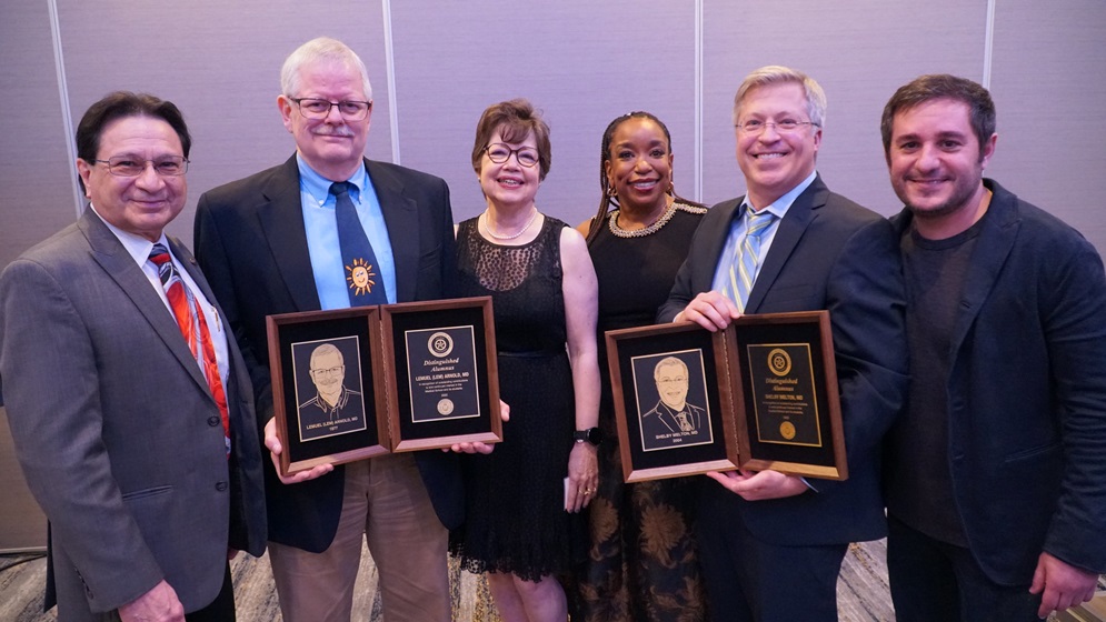 Two Alumni Award winners holding their awards and standing with a group of people.
