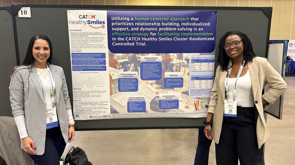 Two presenters stand on either side of a conference poster titled 'CATCH Healthy Smiles,' describing a human-centered implementation approach; both wear badges in a convention hall.