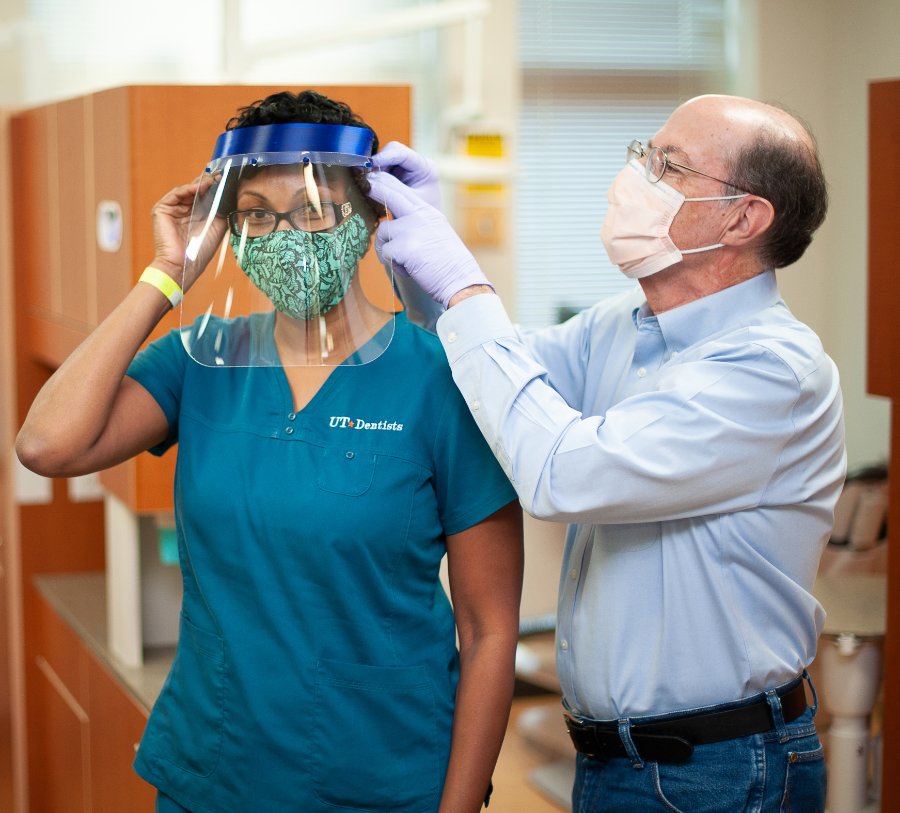 Dr. Scott Makins adjusts a face shield for Dental Assistant Toyia Rose. The shield is one made by his niece, a STEM teacher in Dallas.