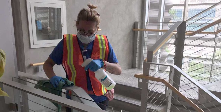 Image of a housekeeping worker wearing gloves and a mask cleaning a stairwell railing at Cizik School of Nursing)