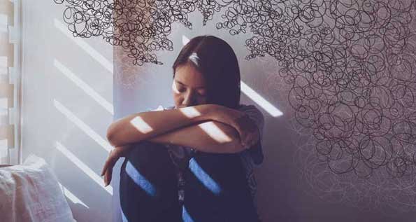 Image of a teen sitting in a darkened room with her head down on her knees. Squiggles representing thoughts surround her.