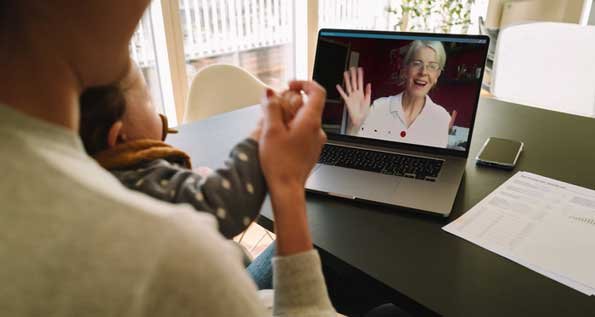 Image of an older woman on a computer screen, waiving at a mother and daughter.