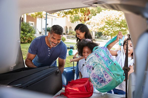 A photograph of a family loading luggage into a car. The photo is by Getty Images.