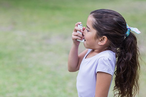 A young girl uses an inhaler to treat asthma. (Photo by Getty Images.)