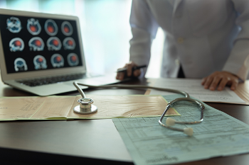 Photo of a screen of brain images and a physician in the background and a stethoscope in the foreground. Photo credit is Getty Images.