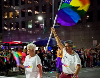 Mary Ann Smith, PhD, marches in the 2018 Houston Pride Parade while holding a Pride flag. (Photo by Meredith Raine)
