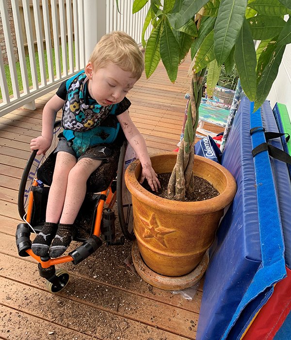 A photo of Levi Hoot in his wheelchair digging in a potted plant.