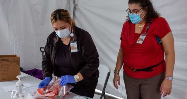Image of two women wearing medical masks and gloves evaluating bags of medical equipment at UT Physicians Multispecialty-Victory. (Photo by Maricruz Kwon/UTHealth)