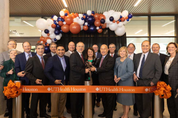 Photo of a group of people standing behind a ribbon, while Dr. Colasurdo holds giant scissors. (Photo by Rogelio Csatro/UTHealth Houston)