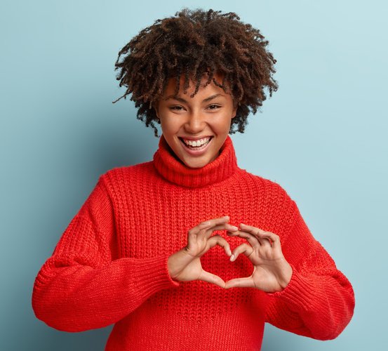 Woman smiles while holding hands in the shape of a heart.