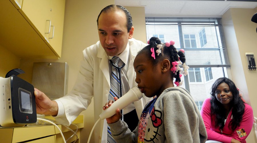 Photo of Dr, Ricardo Mosquera assisting a child as she does a breathing test for a story about clinical providers linking with hospitalists. Photo by Dwight Andrews.