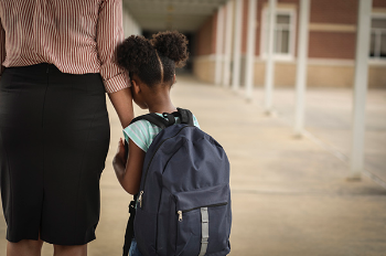 Photo of student holding moms hand in front of school. (Getty Images)