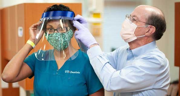 Scott Makins, DDS, MS, adjusts a face shield for Dental Assistant Toyia Rose. The shield is one made by his niece, a STEM teacher in Dallas. (Photo by Brian Schnupp)