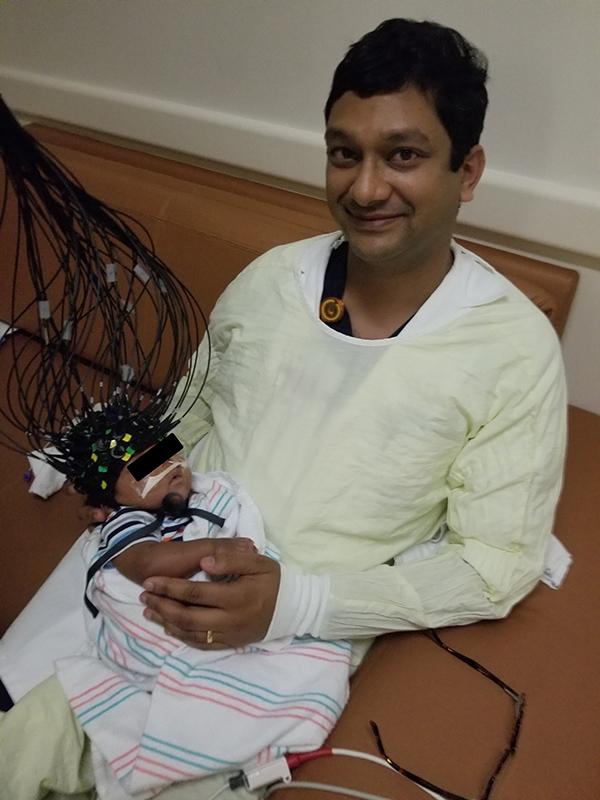 Photo of Manish N. Shah, MD, holding the patient while the Cap-based Transcranial Optical Tomography captures whole-brain imaging in minutes. (Photo credit: Manish N. Shah, MD)