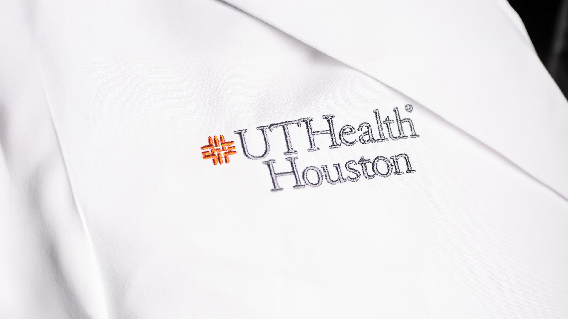Close-up of a white coat with the UTHealth Houston logo embroidered on the chest.