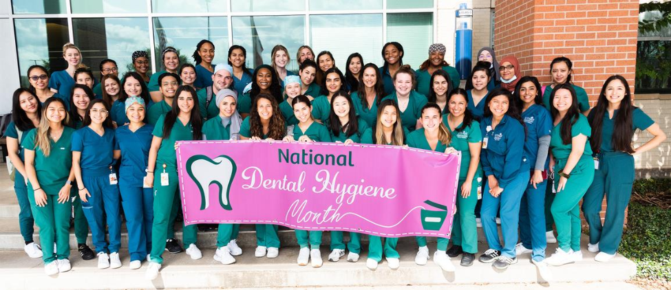 Dental hygiene students gather for a group photo with a National Dental Hygiene Month banner.
