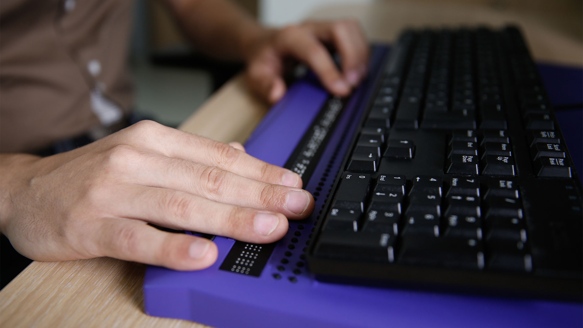 Hands using a computer keyboard with a 'braille' display for accessibility