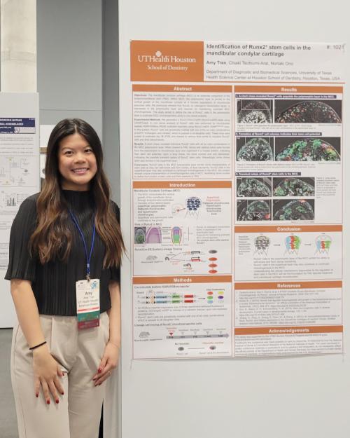 Woman dressed in business casual attire stands next to displayed poster.