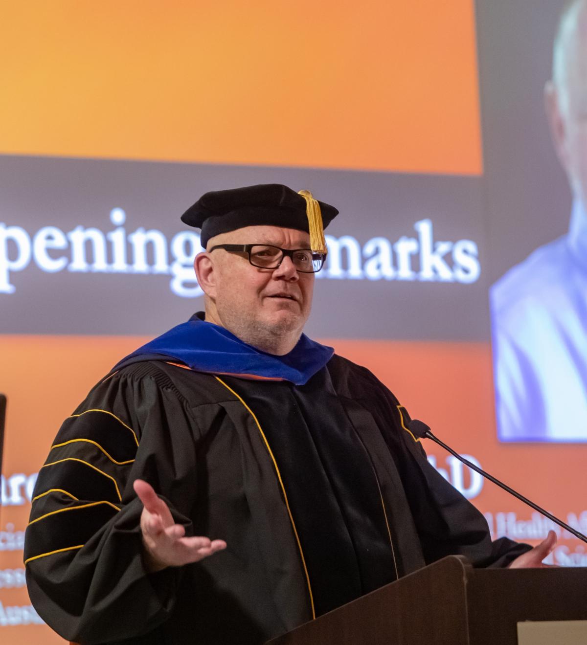 Khol dressed in regalia at podium during commencement