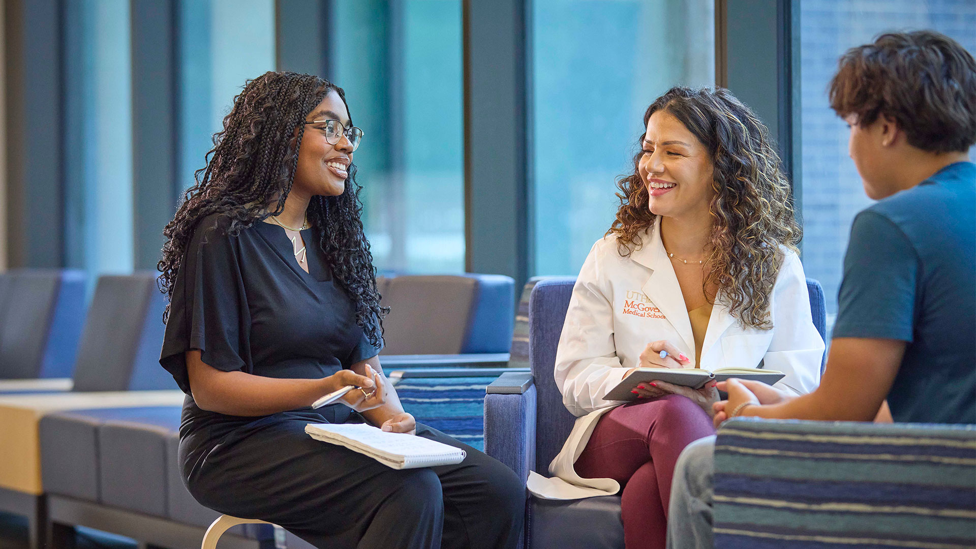 Three students engaged in a collaborative discussion in a modern campus lounge area.