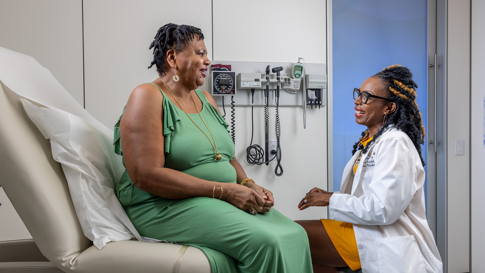 A healthcare provider speaks with a patient in an exam room.