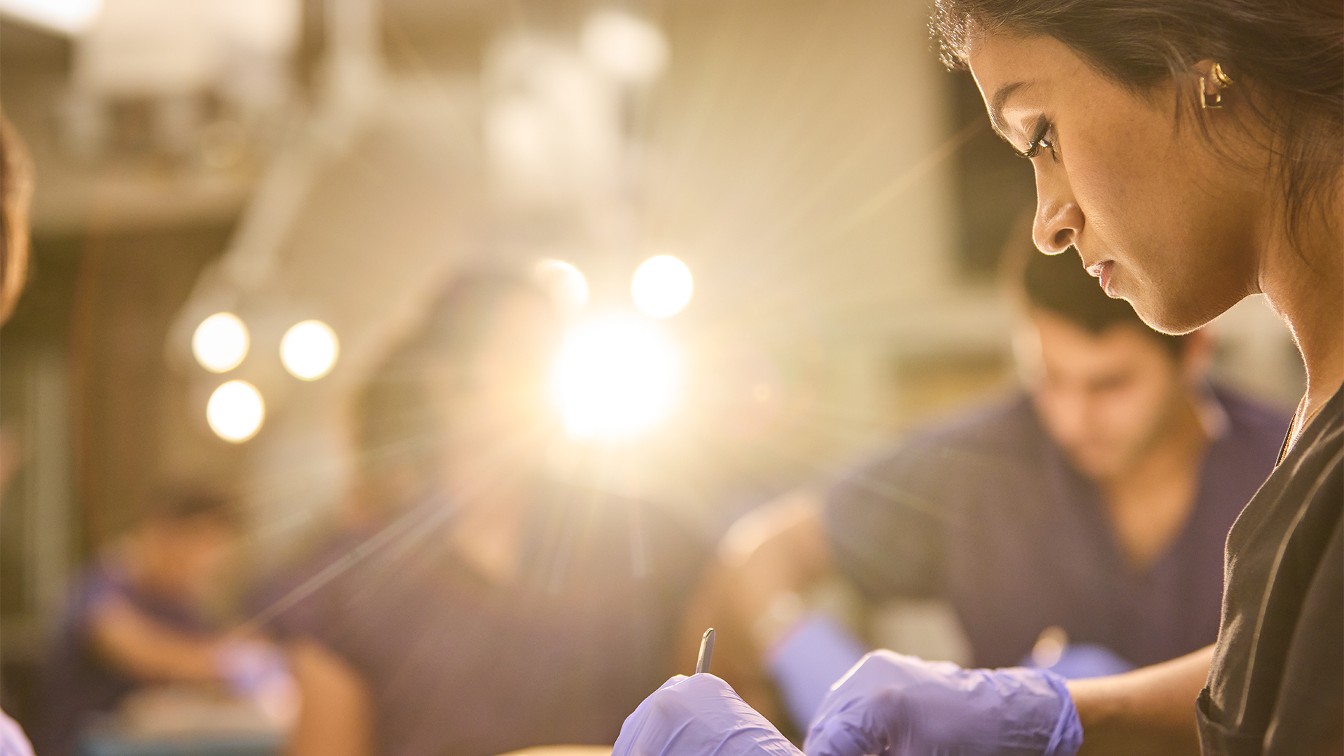 Healthcare trainees wearing gloves perform a clinical procedure under bright surgical lights while focusing on patient care, highlighting hands-on medical education, teamwork, and clinical training at UTHealth Houston.