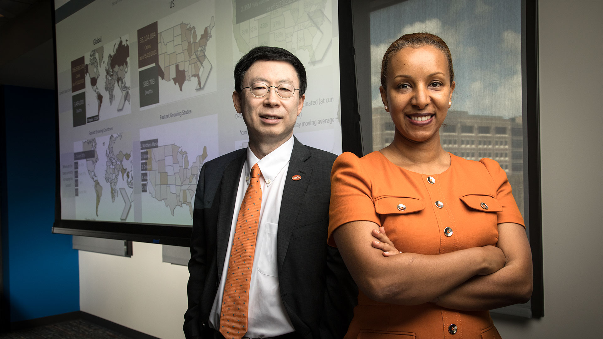 Two faculty members standing in front of presentation screens in an academic or research environment.