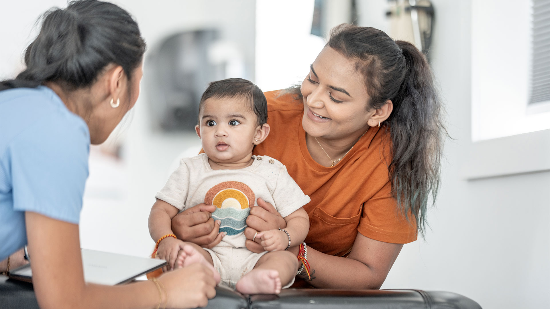 Woman holding her baby while a nurse engages with the baby