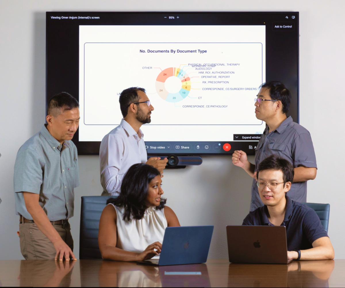Members of the Center for Digital Healthcare Innovation discuss data. Standing, left to right: Luyao Chen; Omer Anjum, PhD; and Xiaoqian Jiang, PhD. Seated: Meera Subash, MD, and Kai Zhang, PhD