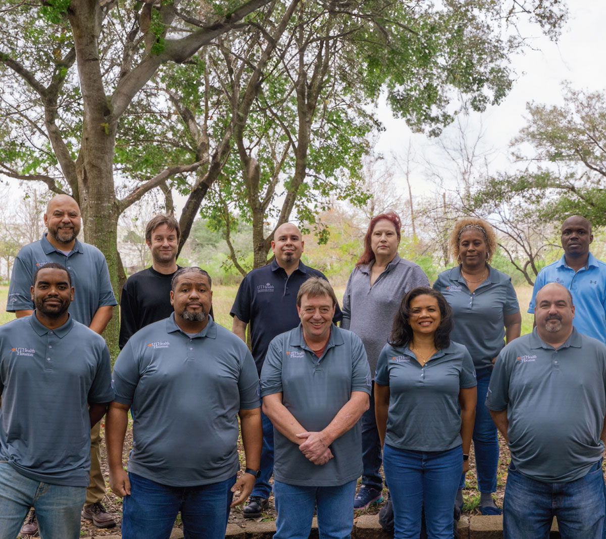 A group of 11 people (David Posado, Naja Brightmon, Alexander Brooks, Tina Bryant, Tiffany Hudson, Olaide Iyiola, Terry Ponder, David Schulman, Brian Thomas, Ruben Valle, and Brian Yegge) in blue and gray polos post together in front of a tree on an overcast day.