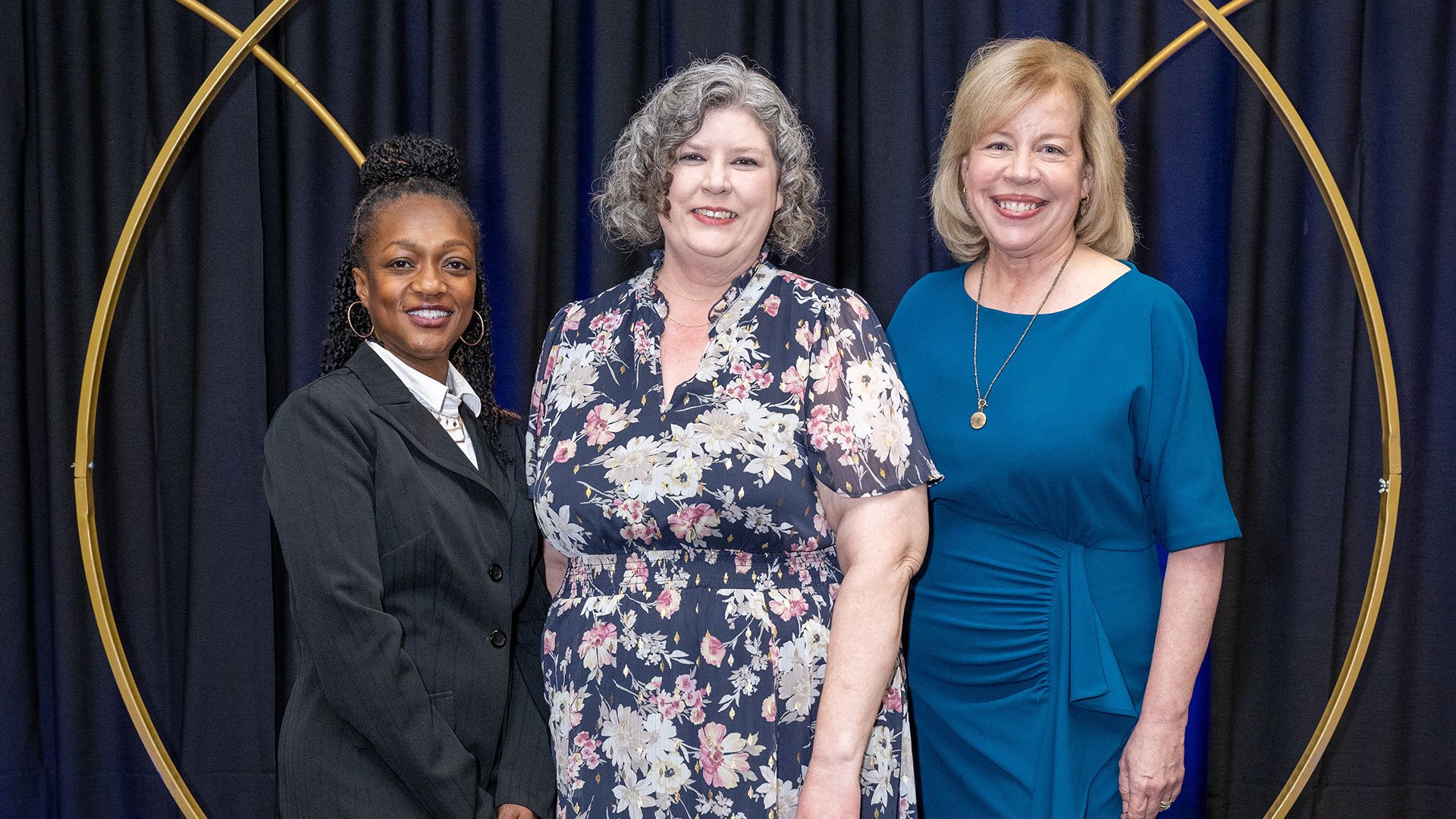 Three women dressed up posing for photo at awards ceremony.