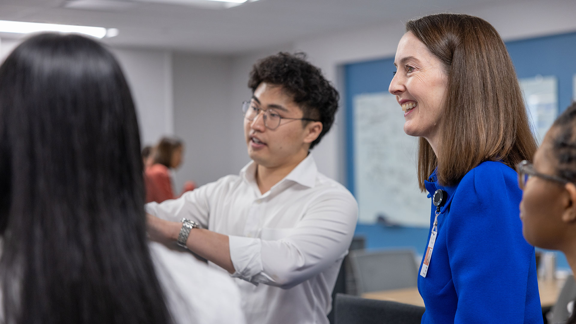 Participants engage in a discussion in a classroom or meeting space as one person gestures toward a presentation while others listen.