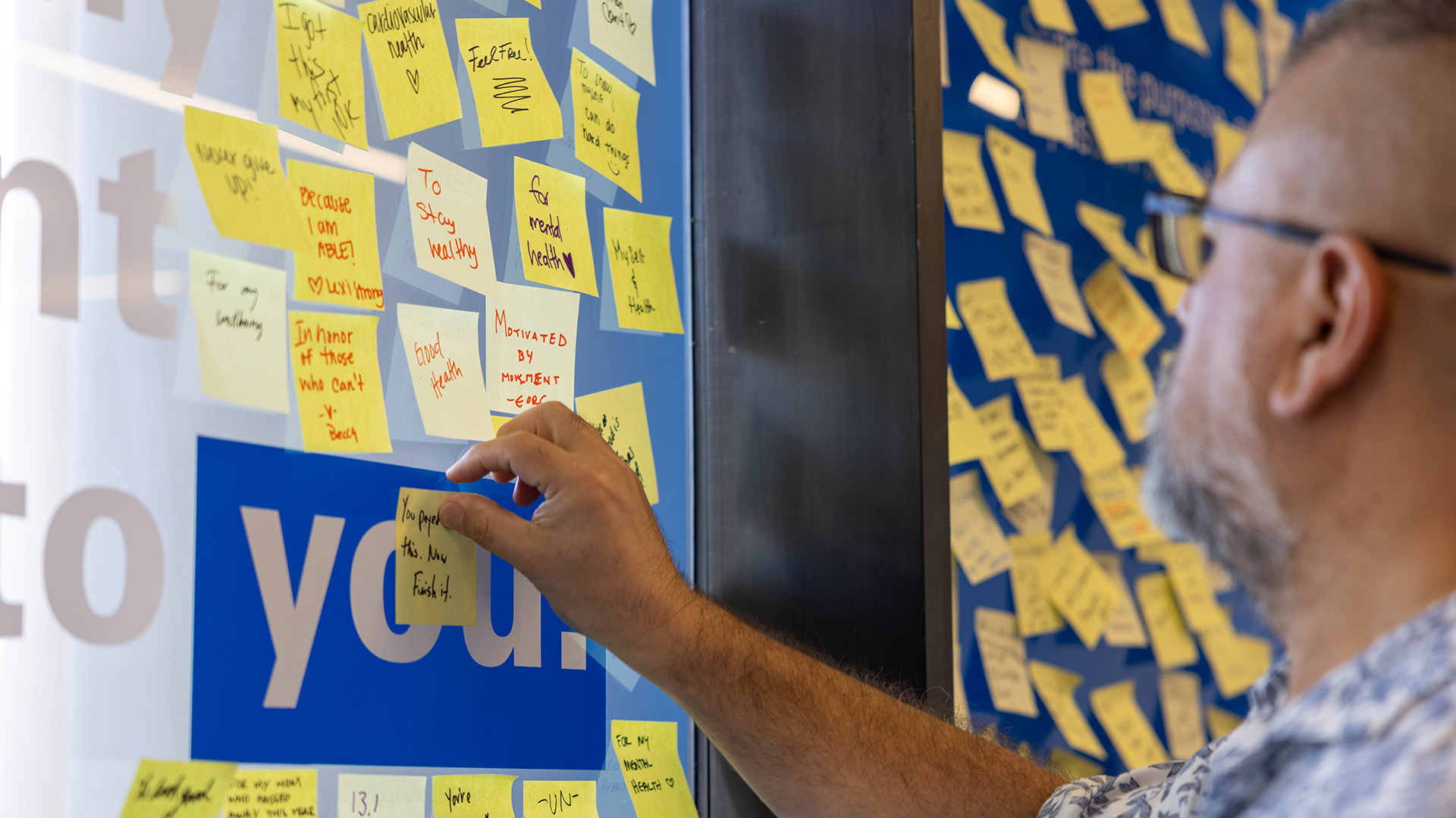Health fair participant adds a handwritten note to a display covered with messages about health and wellness.