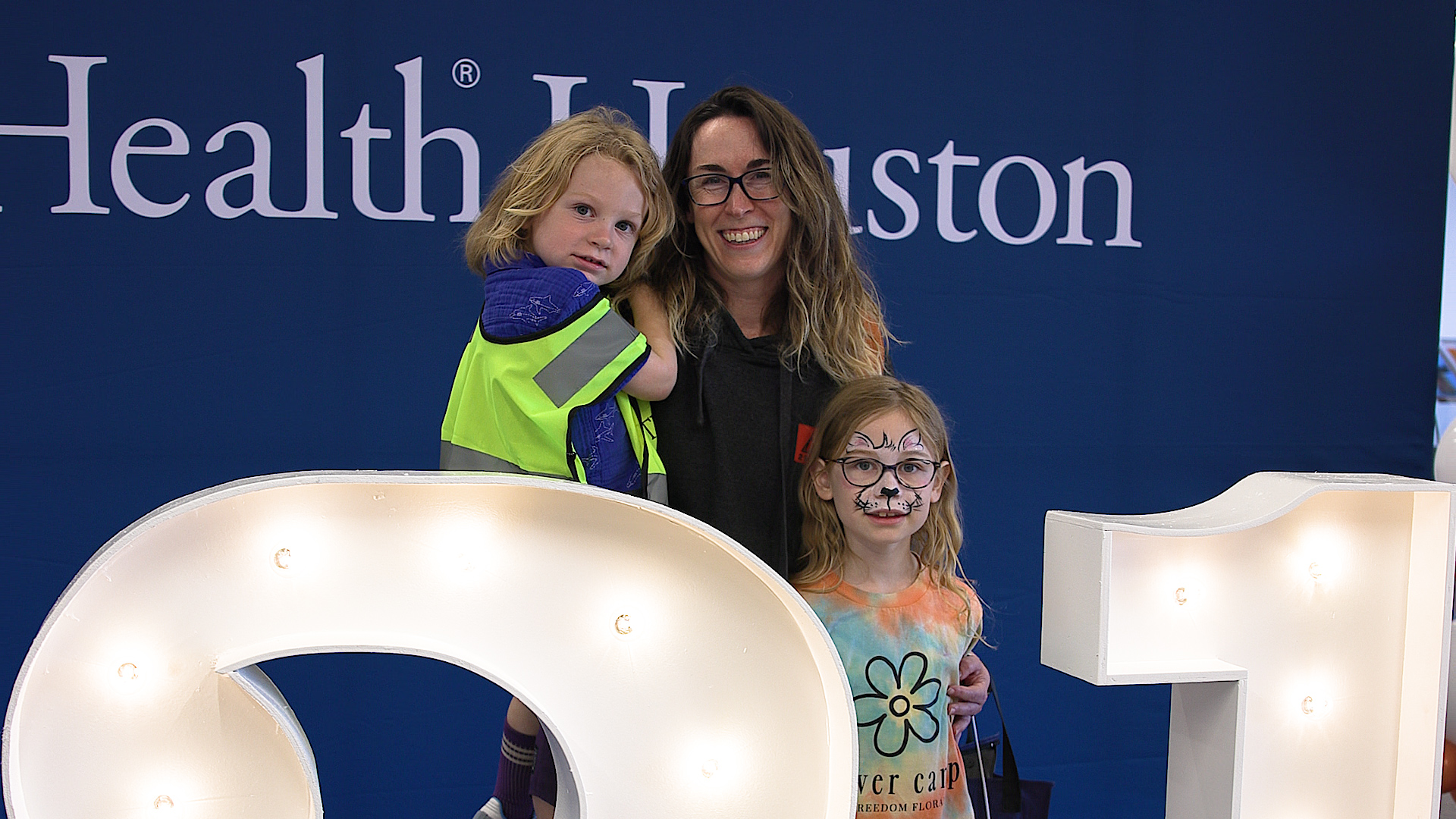 Woman poses with two children in front of a UTHealth Houston display at the health fair.