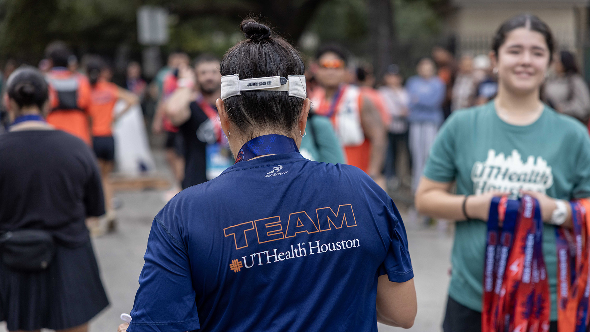 Team UTHealth Houston member stands near the finish area as volunteers distribute medals to race participants.