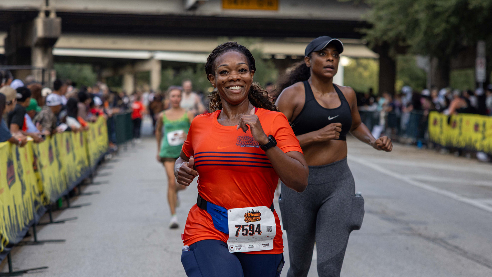 Smiling runner in an orange UTHealth Houston shirt runs toward the finish during the Houston Half Marathon.