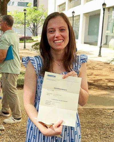 Brooke Bloom smiling and holding her Match Day envelope while standing outdoors.