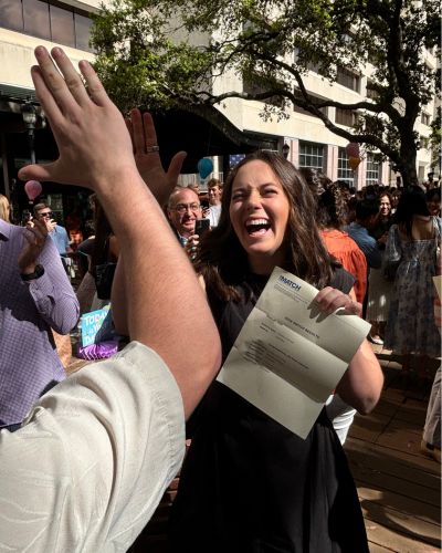 Priscilla &ldquo;Polly&rdquo; Haff smiling and high-fiving someone while holding her Match Day envelope outdoors, surrounded by a crowd of celebrating classmates at McGovern Medical School.