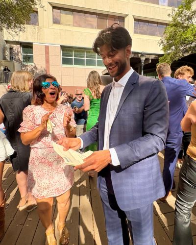 Neil Jayarajan smiling and looking down at his Match Day envelope while standing among celebrating classmates outdoors.