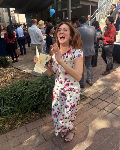 Sydney Keatts smiling and clapping while holding her Match Day envelope outdoors, surrounded by classmates and a festive crowd.
