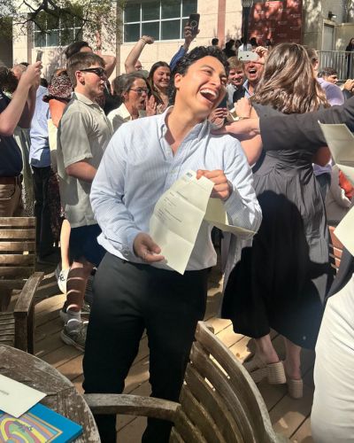 Eloy Lozoya smiling and holding his Match Day envelope while celebrating in a crowd of cheering classmates outdoors.