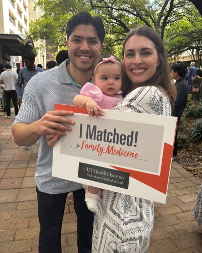 Emily Peel smiling while holding a &ldquo;I Matched&rdquo; sign alongside family members and a baby during an outdoor celebration.