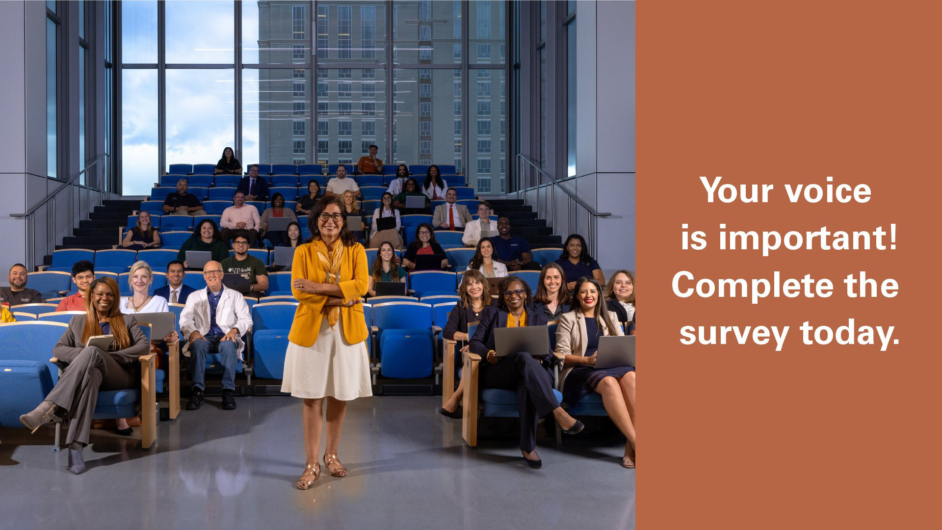 Group of employees in a modern auditorium with text reading, “Your voice is important! Complete the survey today.